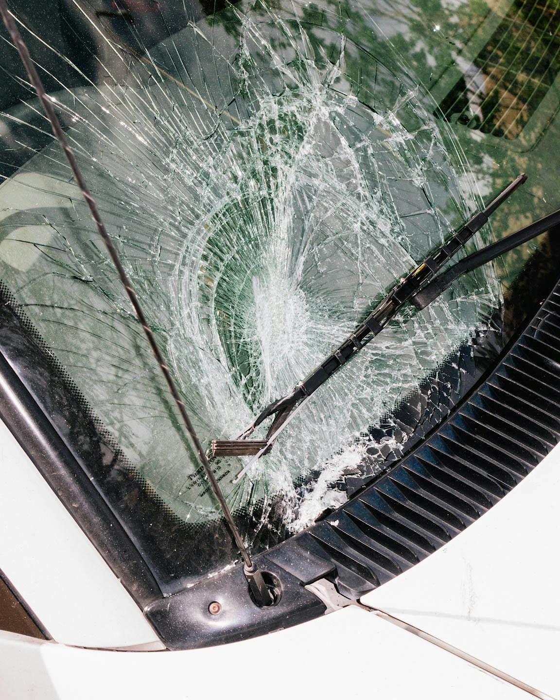A white vehicle with a badly cracked (nearly shattered) windshield.